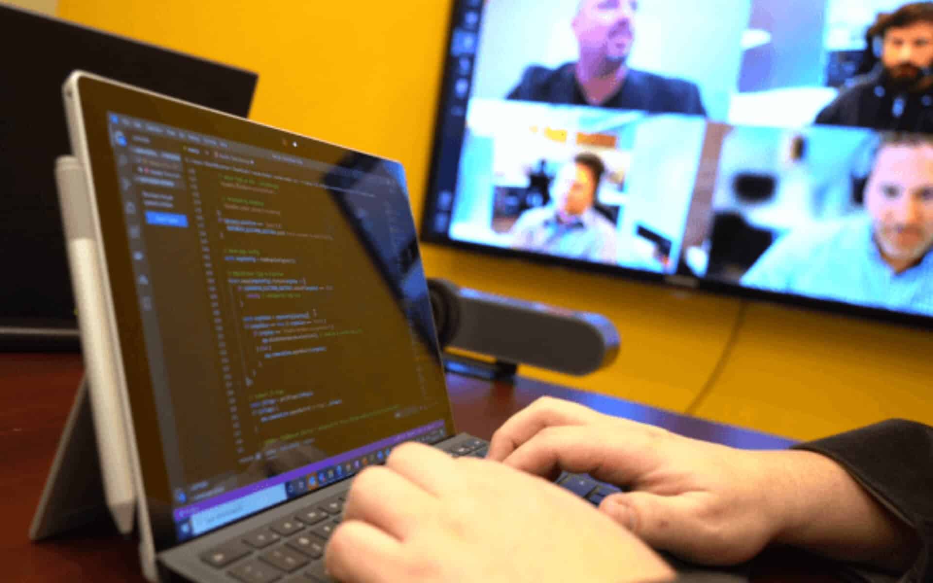 Some of the MERAK Systems team attend developer meeting on video conferencing while one types code on a laptop